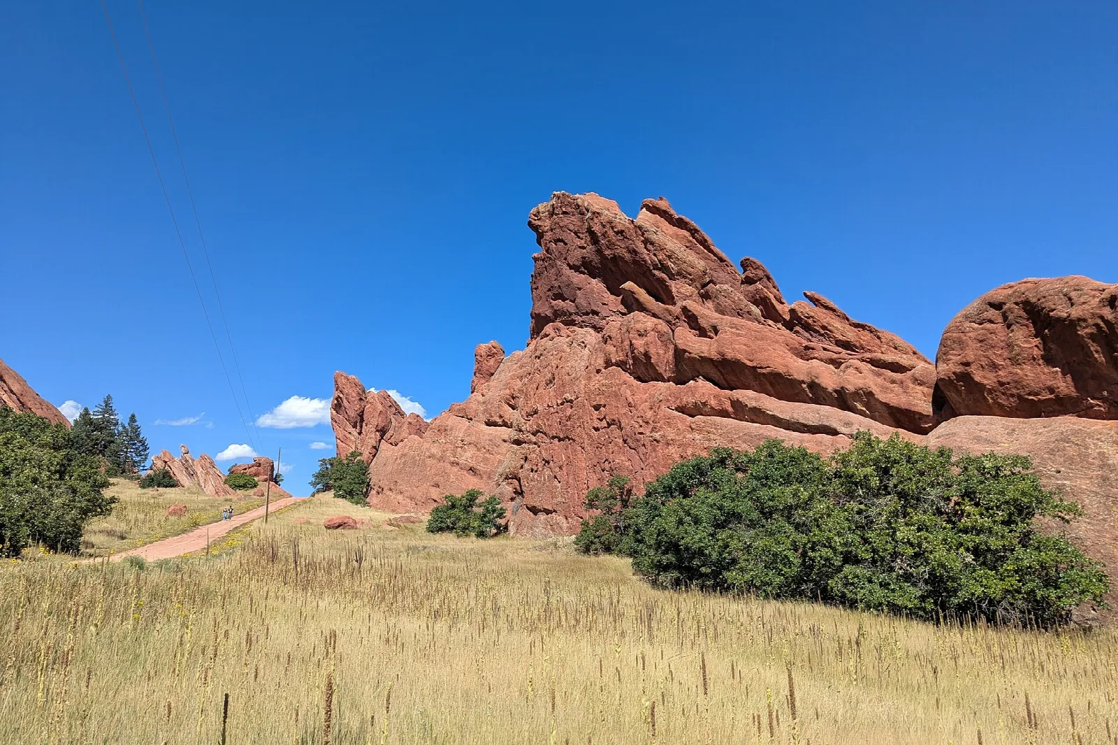 Red sandstone outcrop above golden grass with a dirt path and blue sky