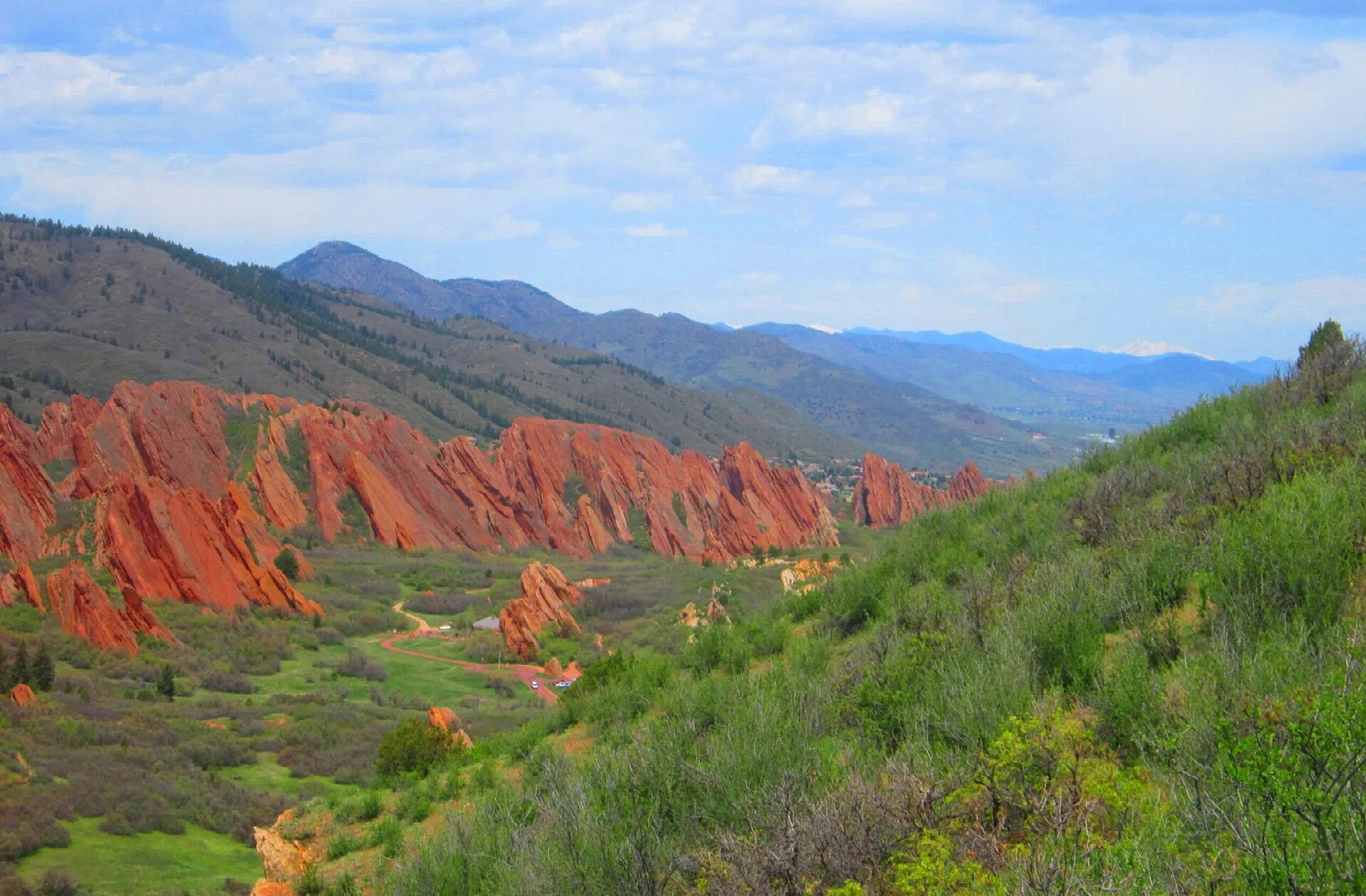 A valley of red rock ridges with green slopes and distant mountains