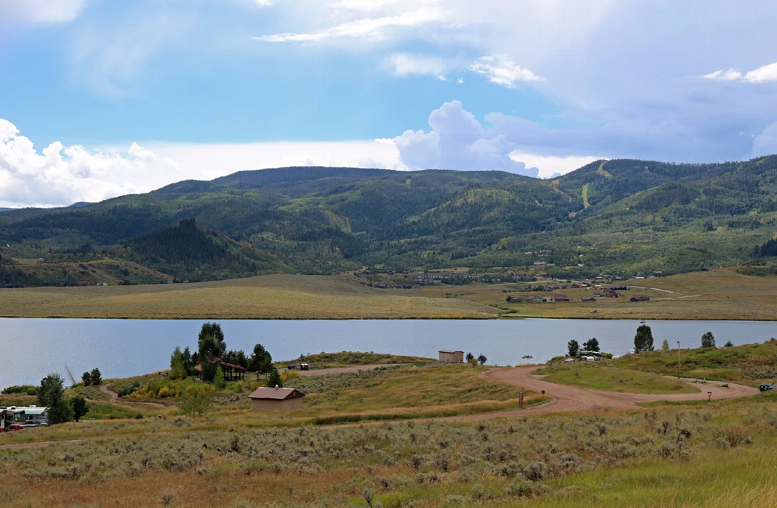 Reservoir below sage-covered hills and green mountains under a cloudy sky