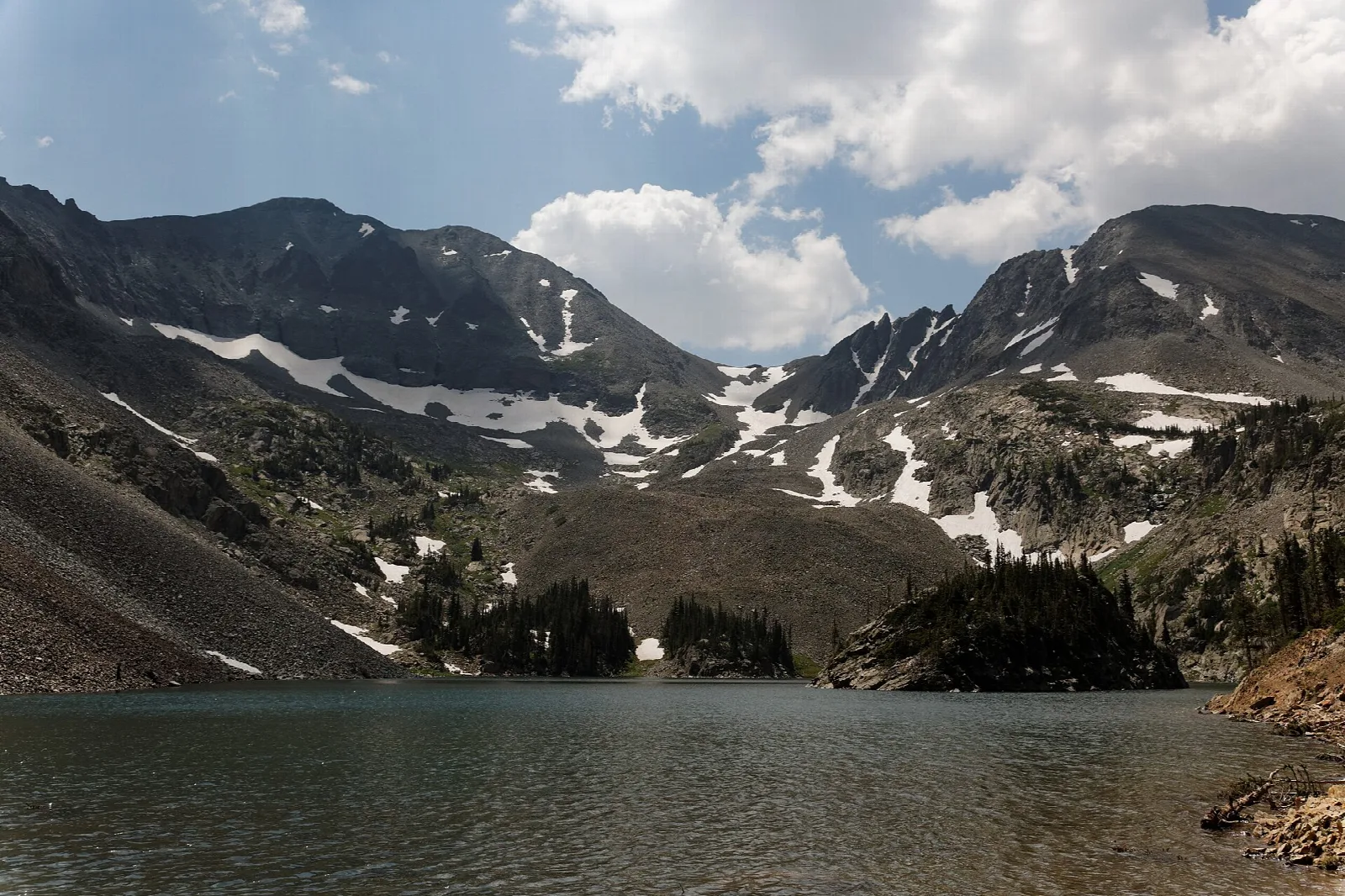 Dark alpine lake below rugged peaks streaked with snow