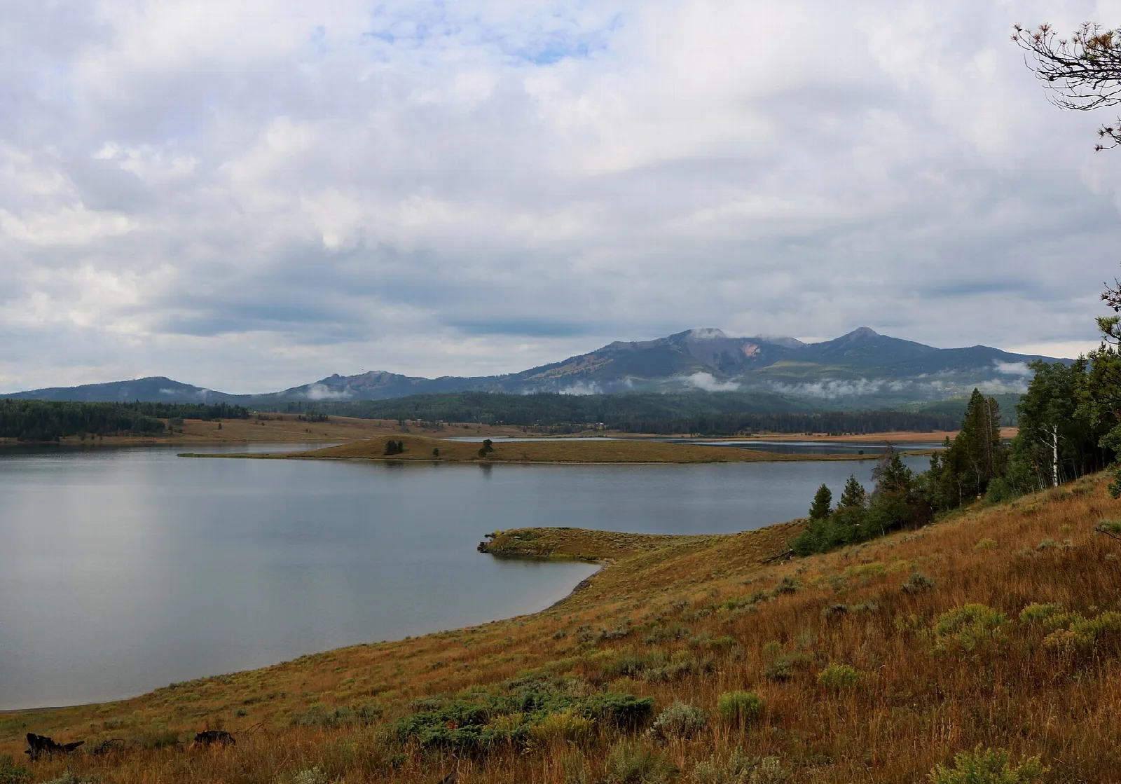 Calm lake edged by a brown grassy slope with a mountain ridge in the distance