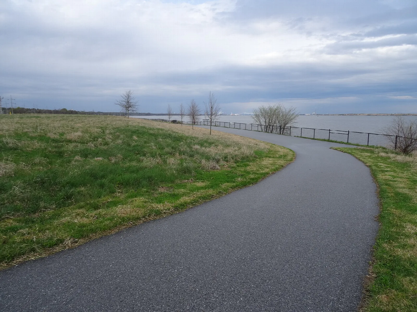 Curving paved path along a grassy bank beside the river