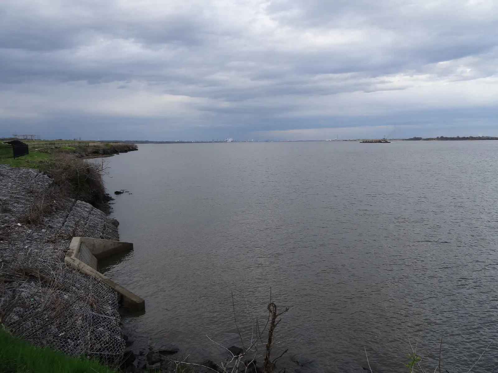 Wide gray stretch of the Delaware River under cloudy sky, with a rocky bank at left
