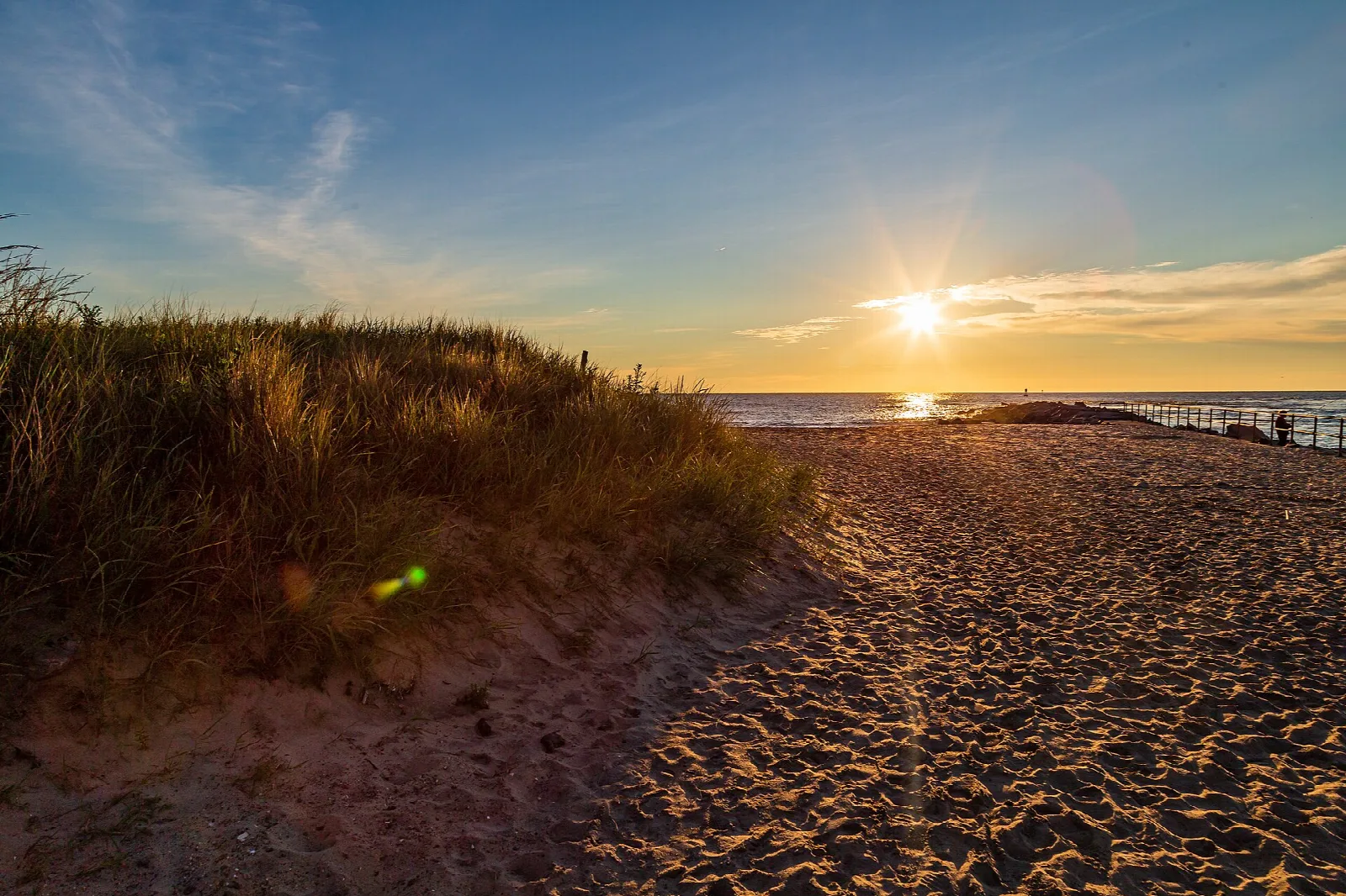 Sun low over a sandy path through dune grass toward the ocean