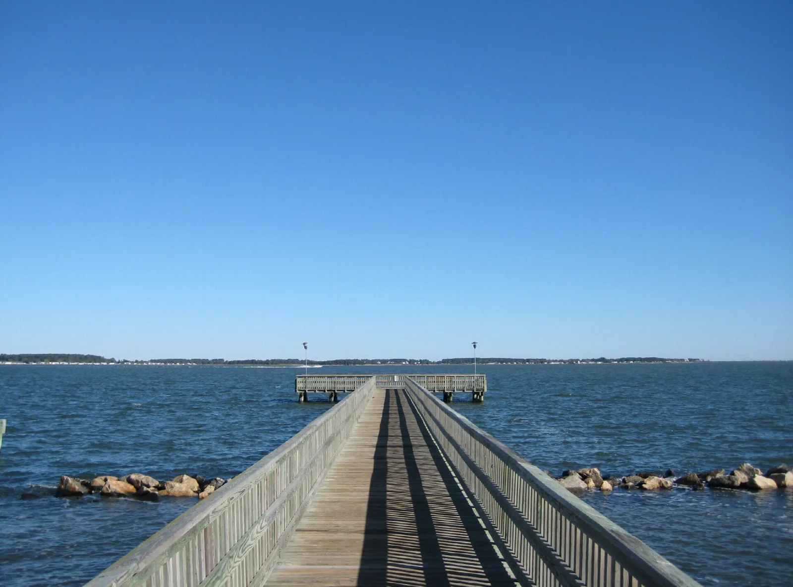Wooden pier stretching out over blue bay water under a clear sky