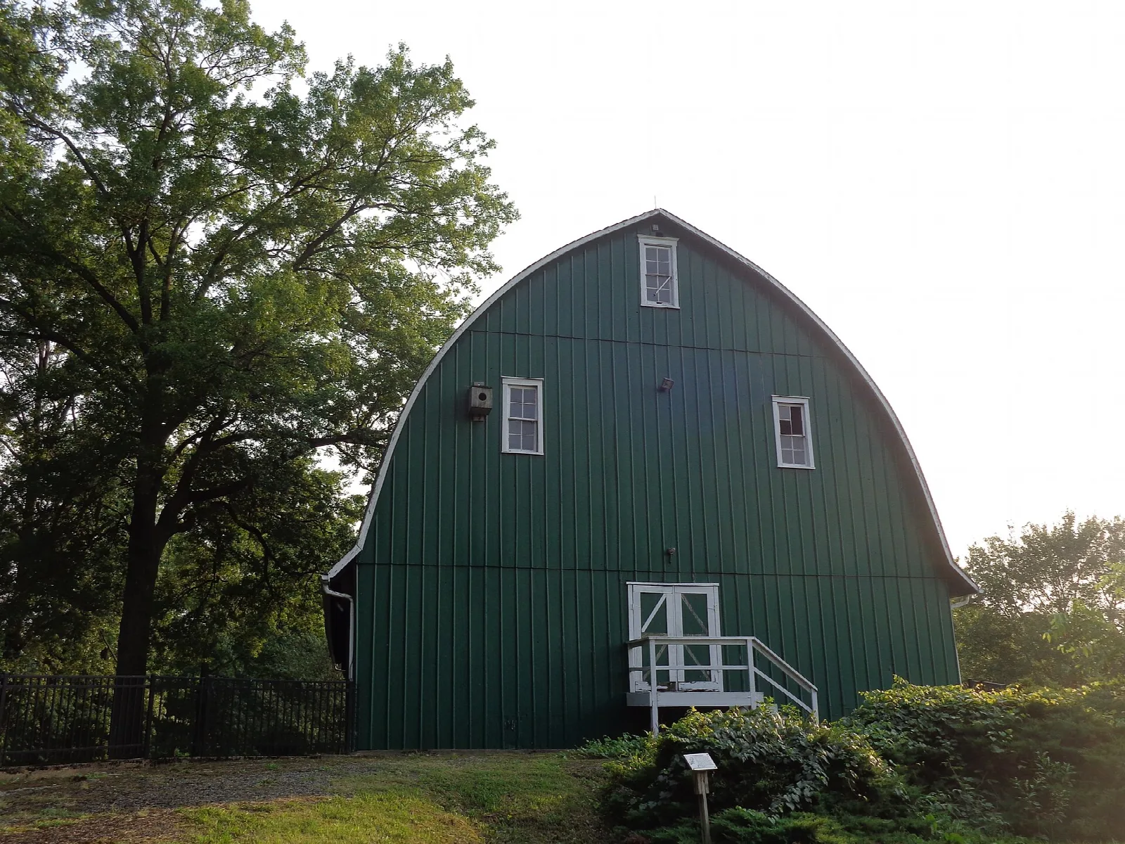Large green gambrel-roofed barn among trees