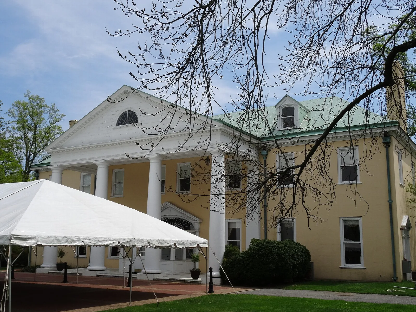 Front porch and columns of a yellow mansion with a white tent beside it