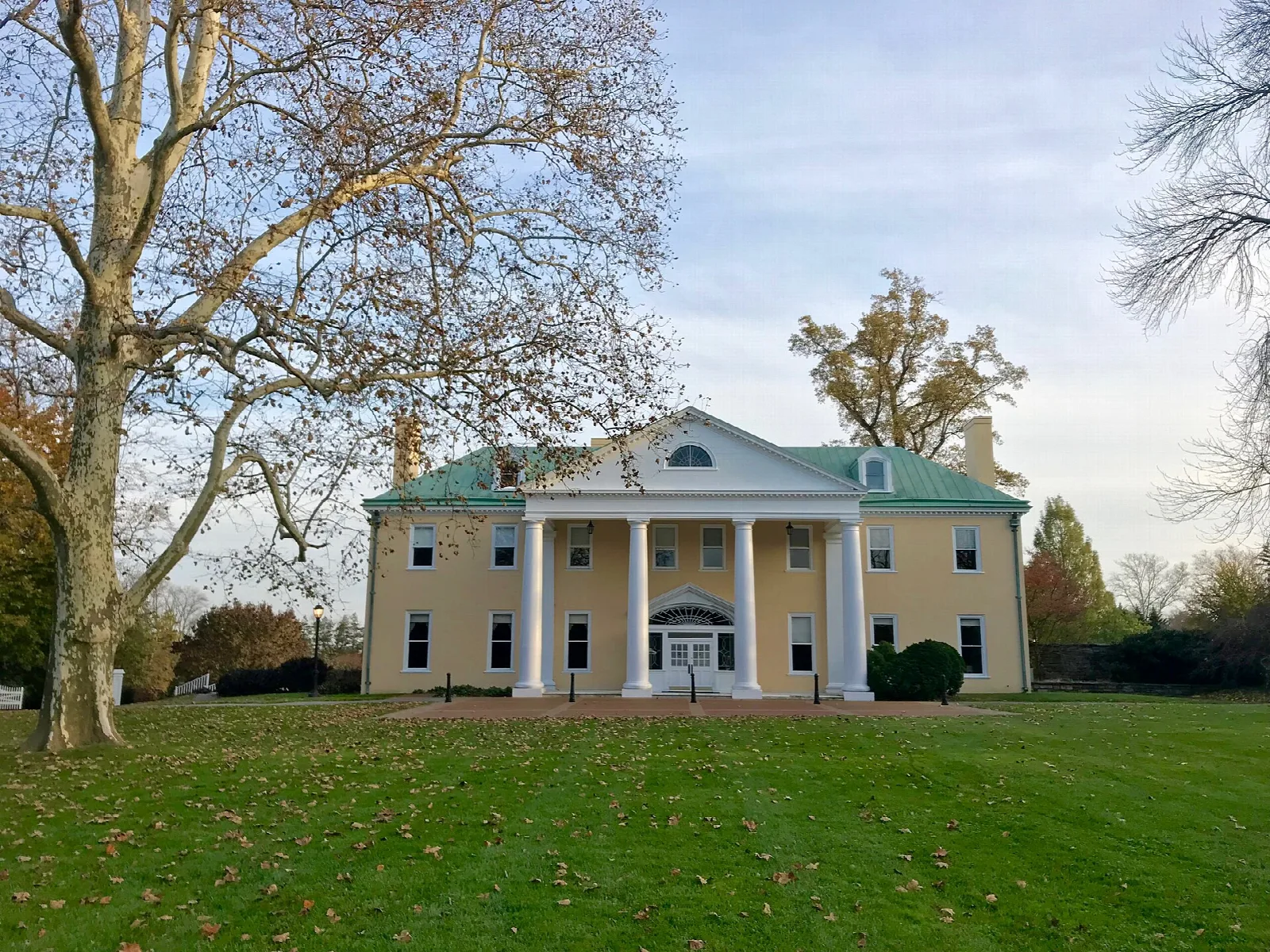 Yellow columned mansion across a wide green lawn with autumn trees