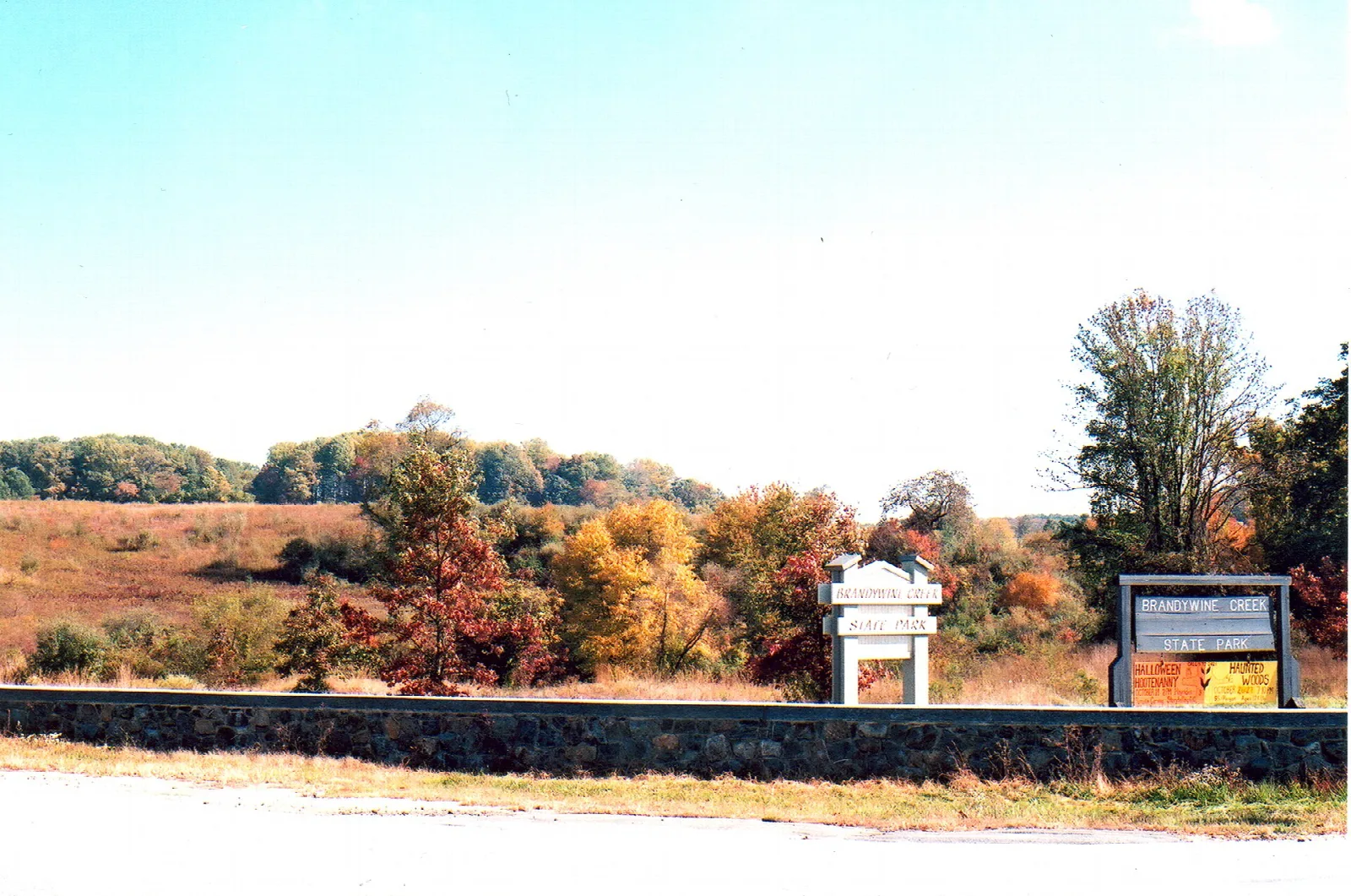 Autumn meadow with orange trees and park signs along a low stone wall