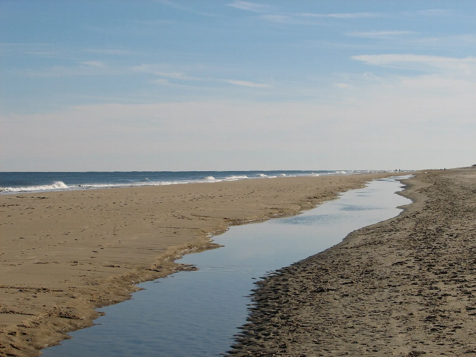 Wide sandy beach with a tidal pool and ocean in the distance