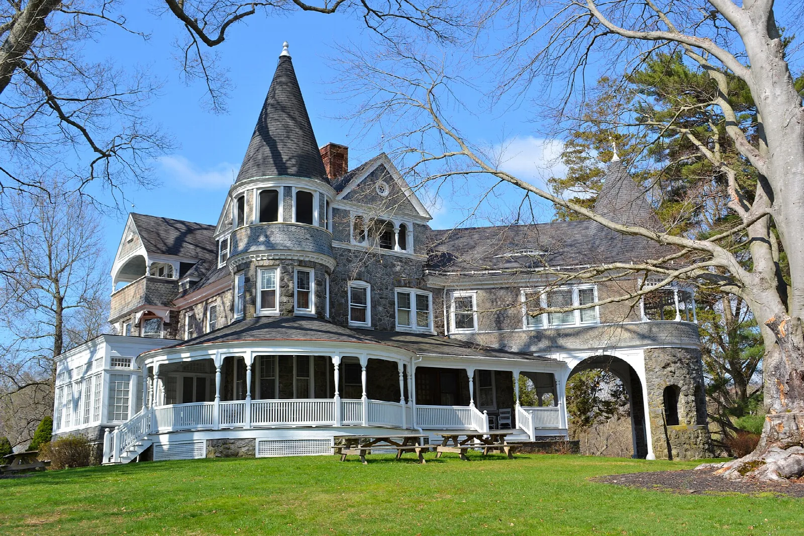 Gray stone Queen Anne house with a turret and wraparound porch on a lawn