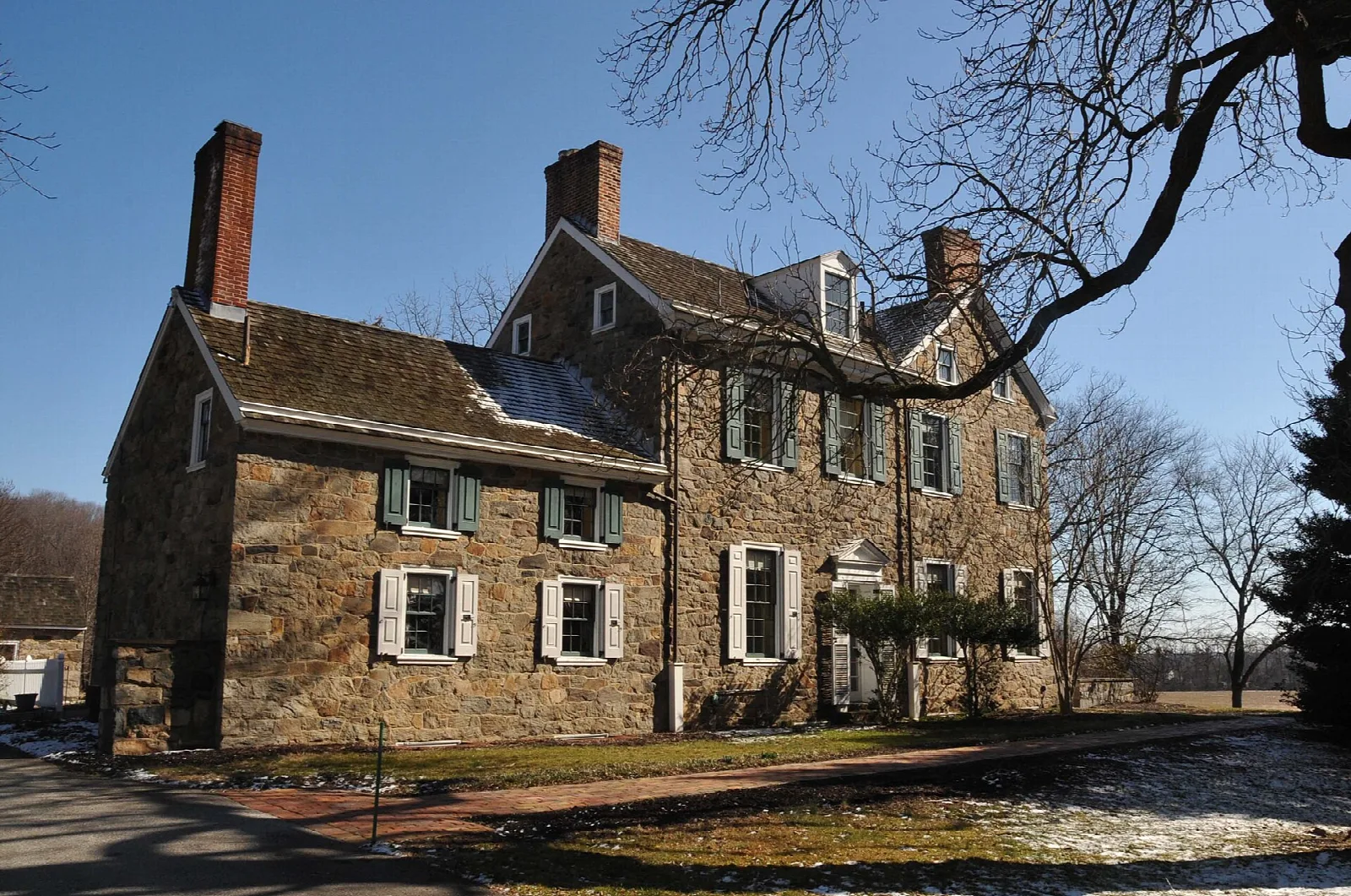 Large stone house with chimneys and a gabled roof under a blue sky