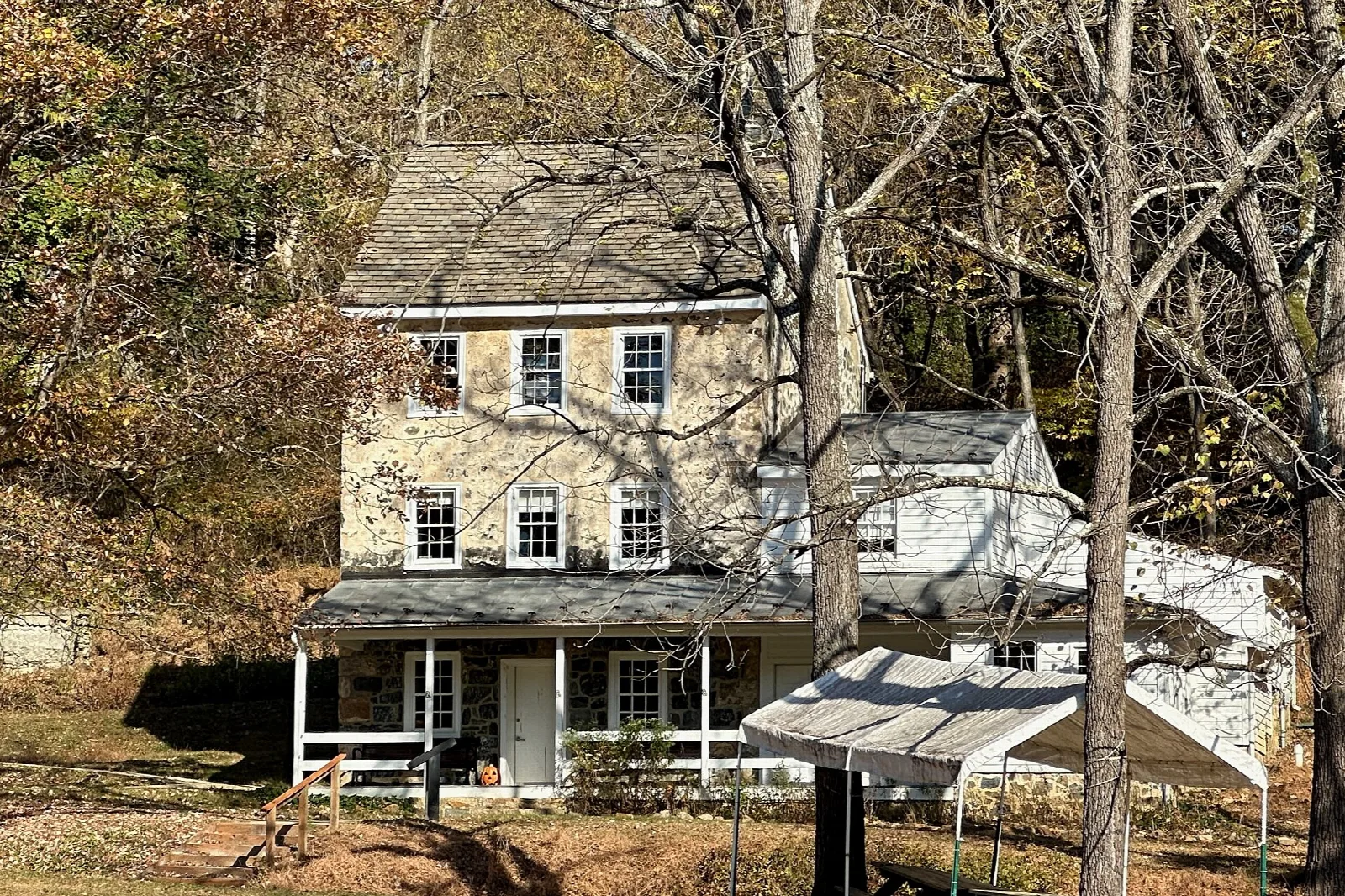 Old stone farmhouse with a porch among autumn trees