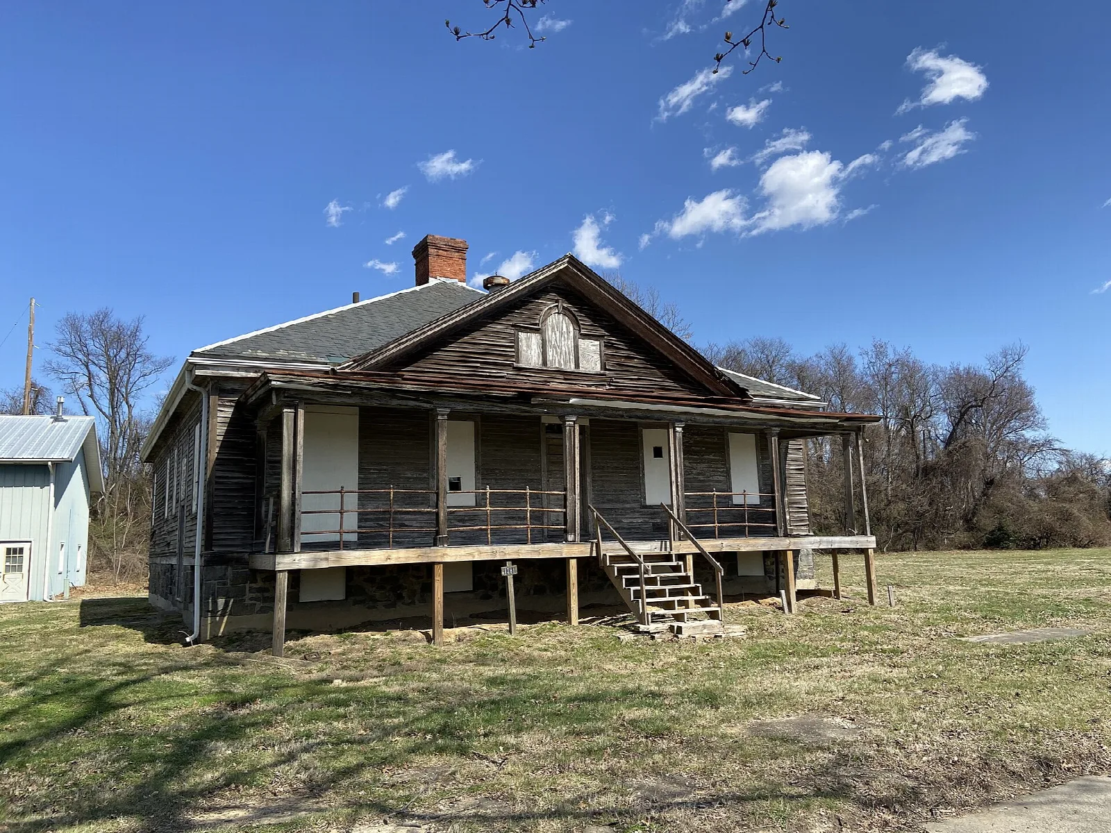 Weathered wooden house with a porch on a grassy field