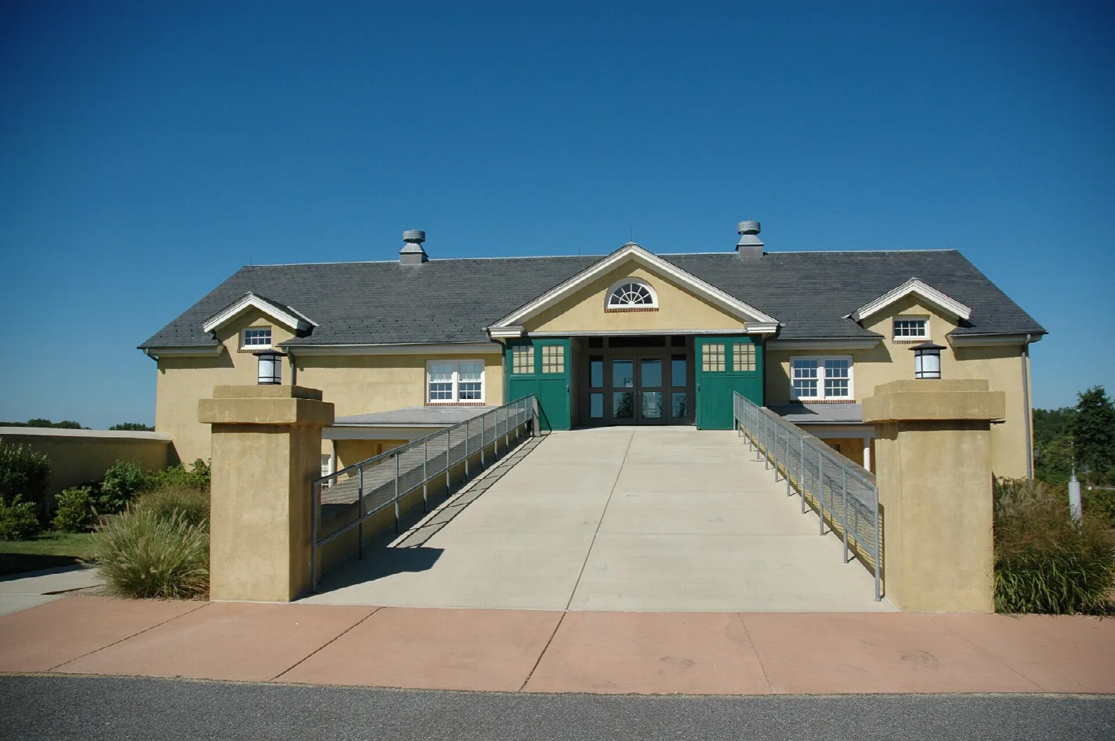 Tan dairy barn with green doors at the end of a walkway