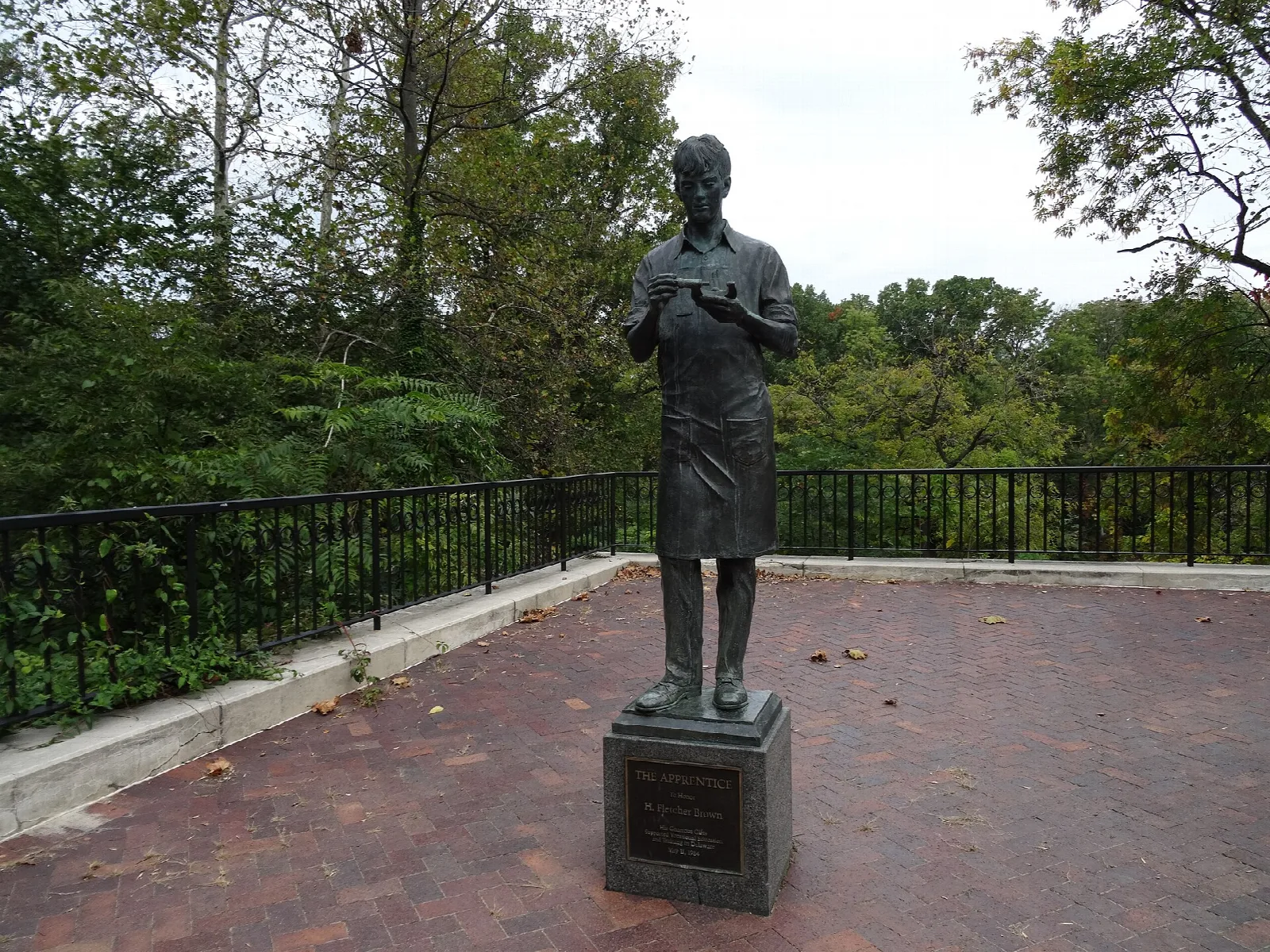 Bronze statue on a brick terrace with a railing and trees