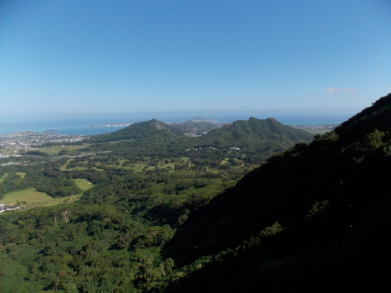 Green valley and distant coast seen from a cliff edge under clear blue sky
