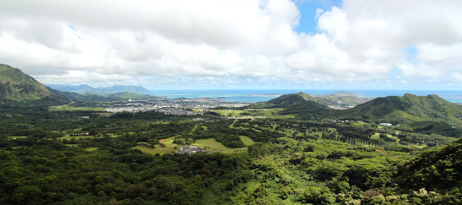 Wide panorama of green valley, hills and ocean horizon under clouds