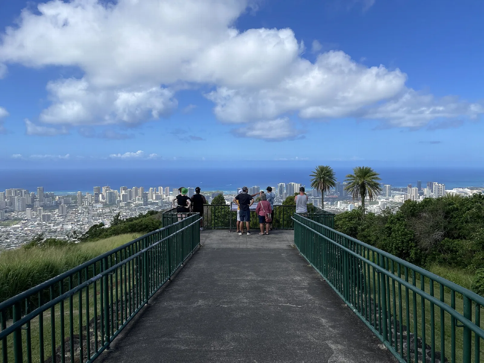 Paved lookout walkway with green railings leading toward the ocean and city