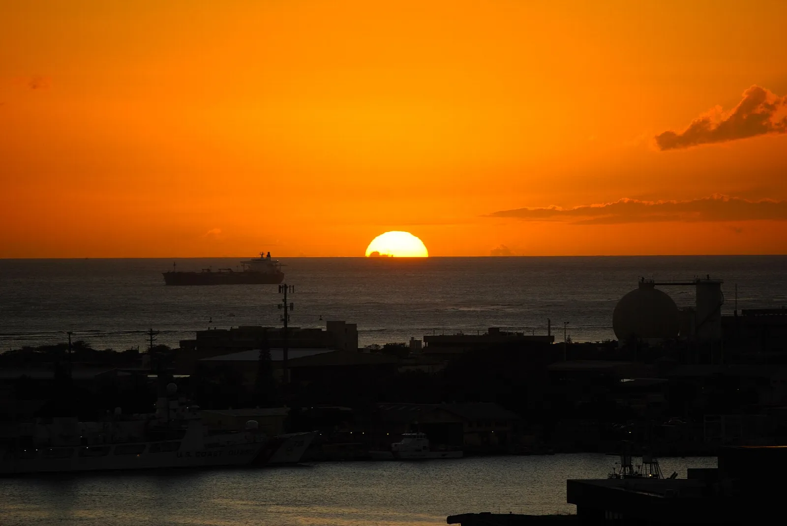 Orange sun setting over the harbor, with dark shoreline shapes below
