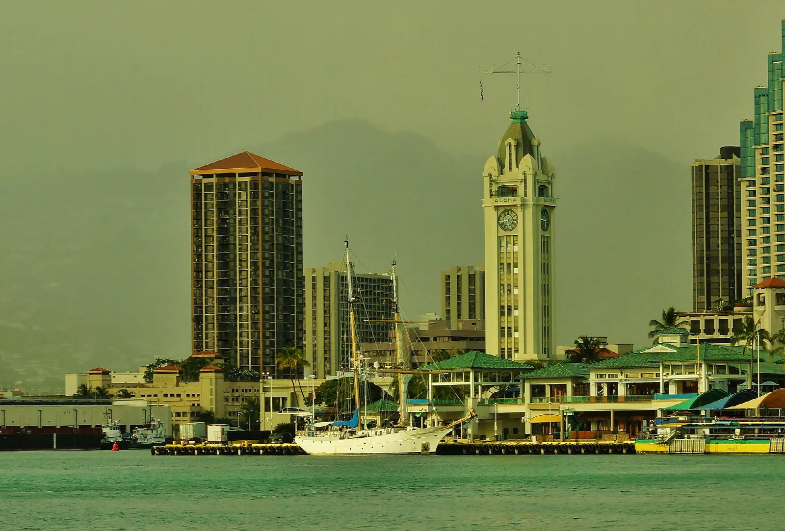 Aloha Tower and downtown buildings across green harbor water
