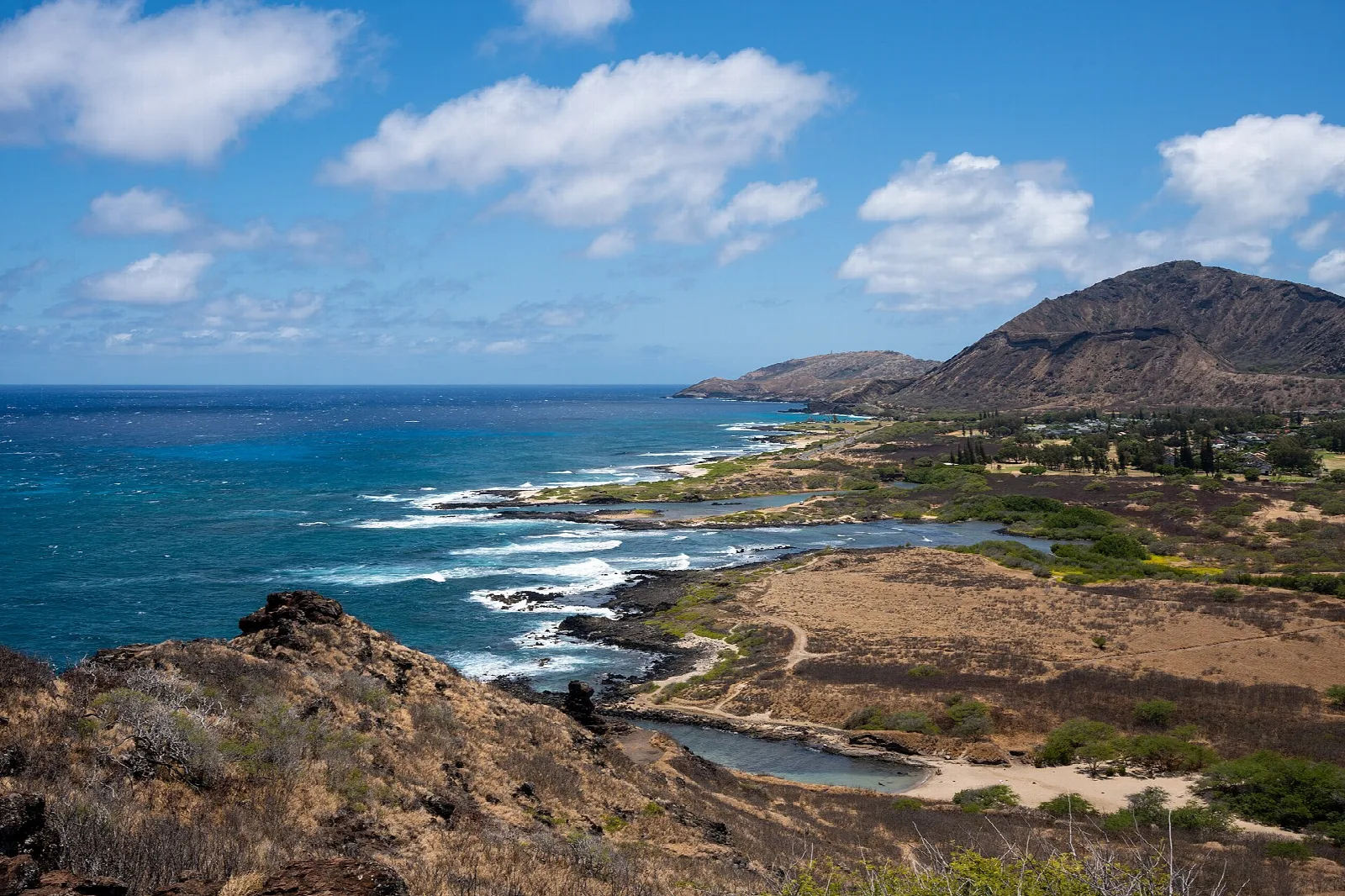 Rocky coastline with white surf and Koko Head in the distance under blue sky