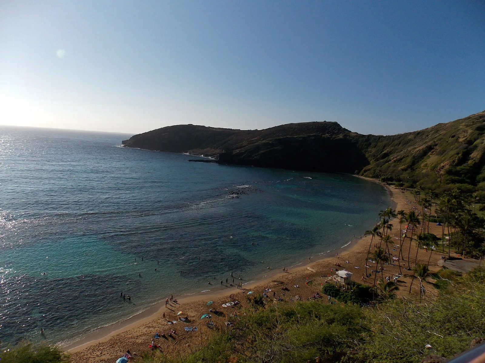 Calm blue bay with a sandy shoreline seen from a green hillside