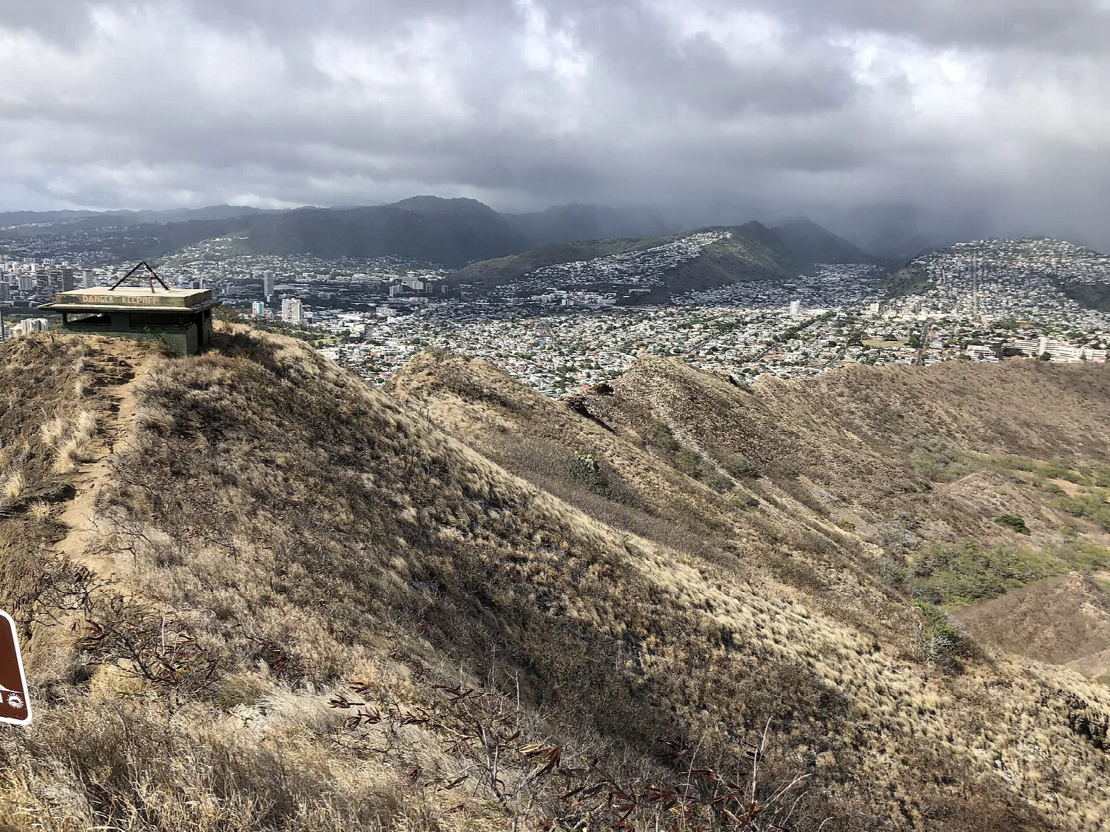 Dry crater ridge sloping toward the city, with a lookout structure on the left
