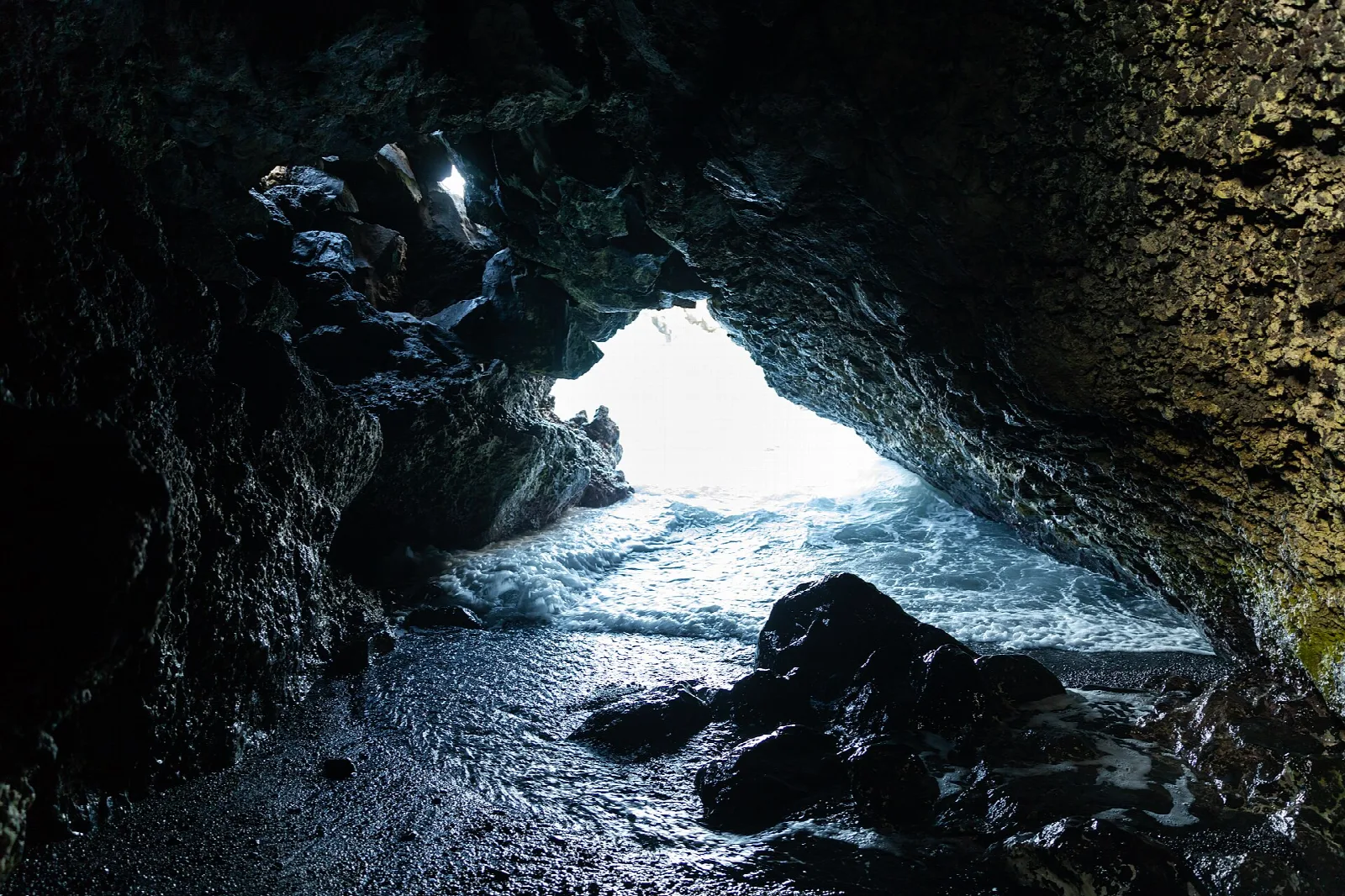 Dark lava tunnel opening onto the sea, with a rocky floor