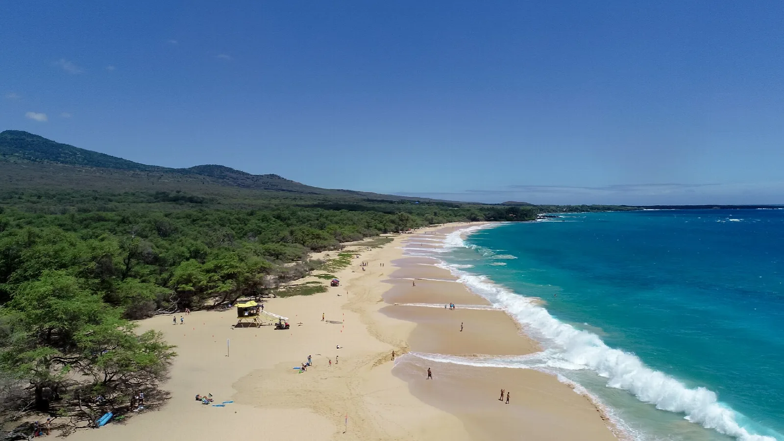 Long sandy beach with breaking waves and green hills behind