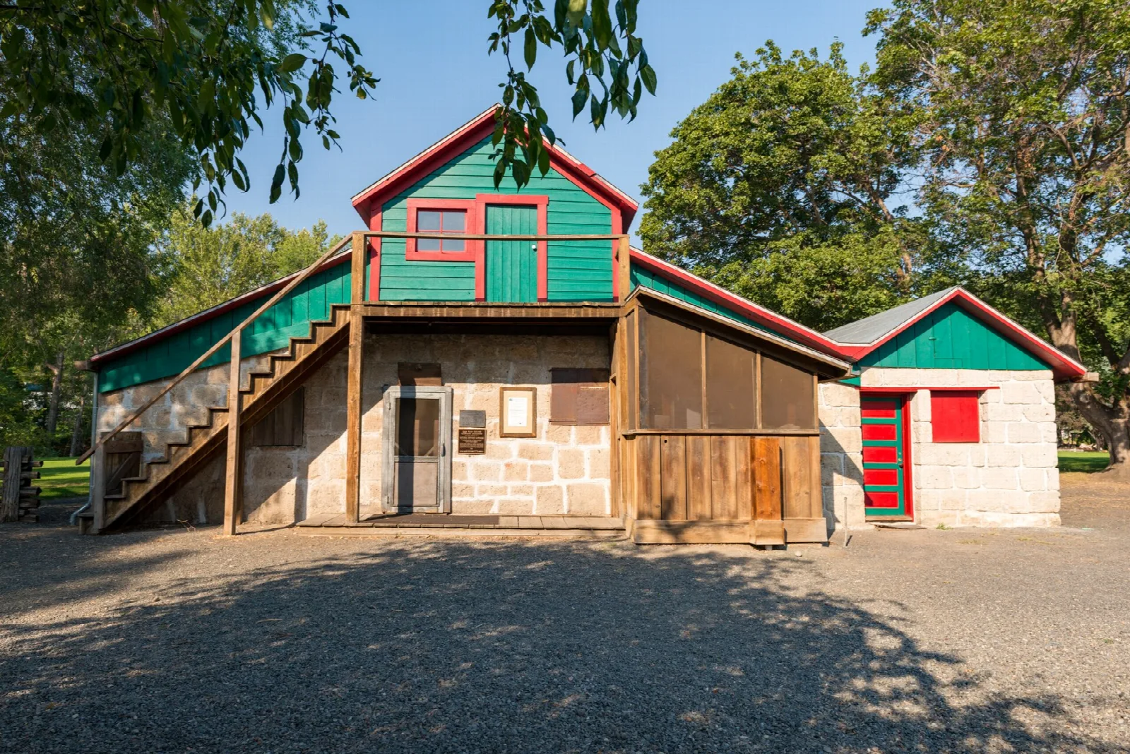 Green-trimmed stone building with a wooden stair and screened porch