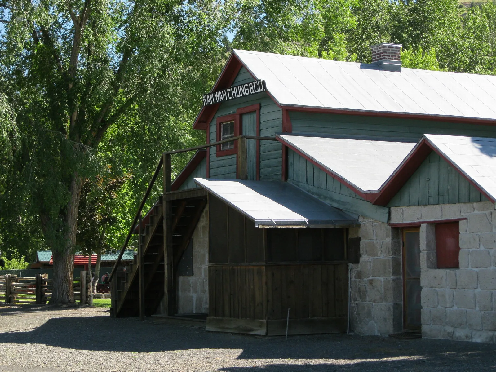 Two-story stone building with a stair and metal roof among willows