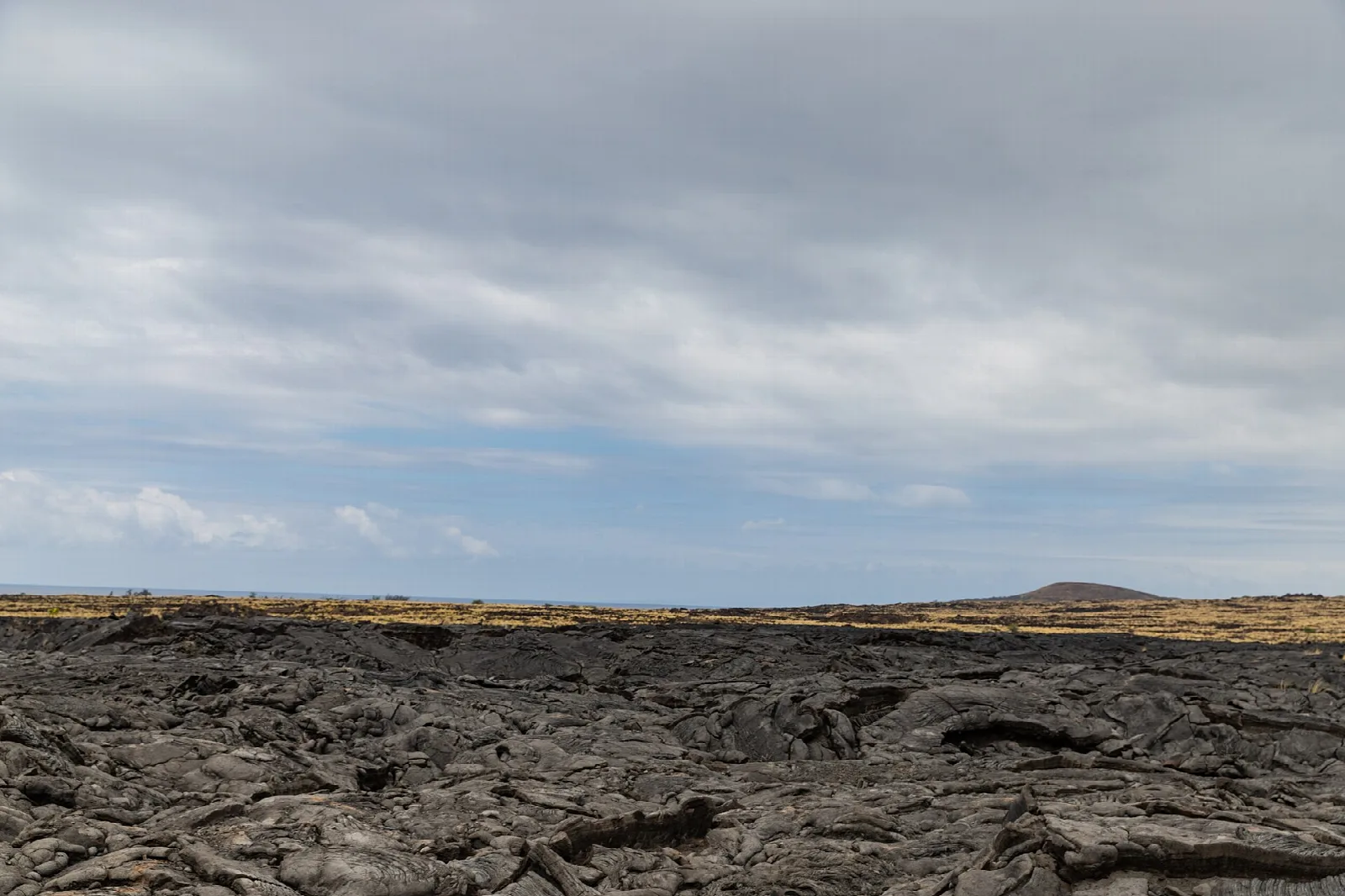 Wide black lava field under a cloudy sky