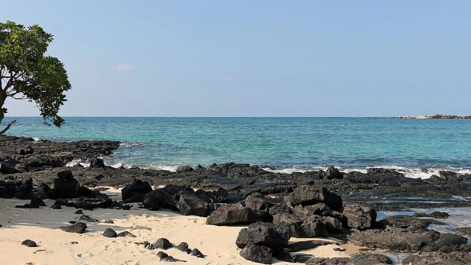 Lava rock shoreline with a small sandy cove and blue water