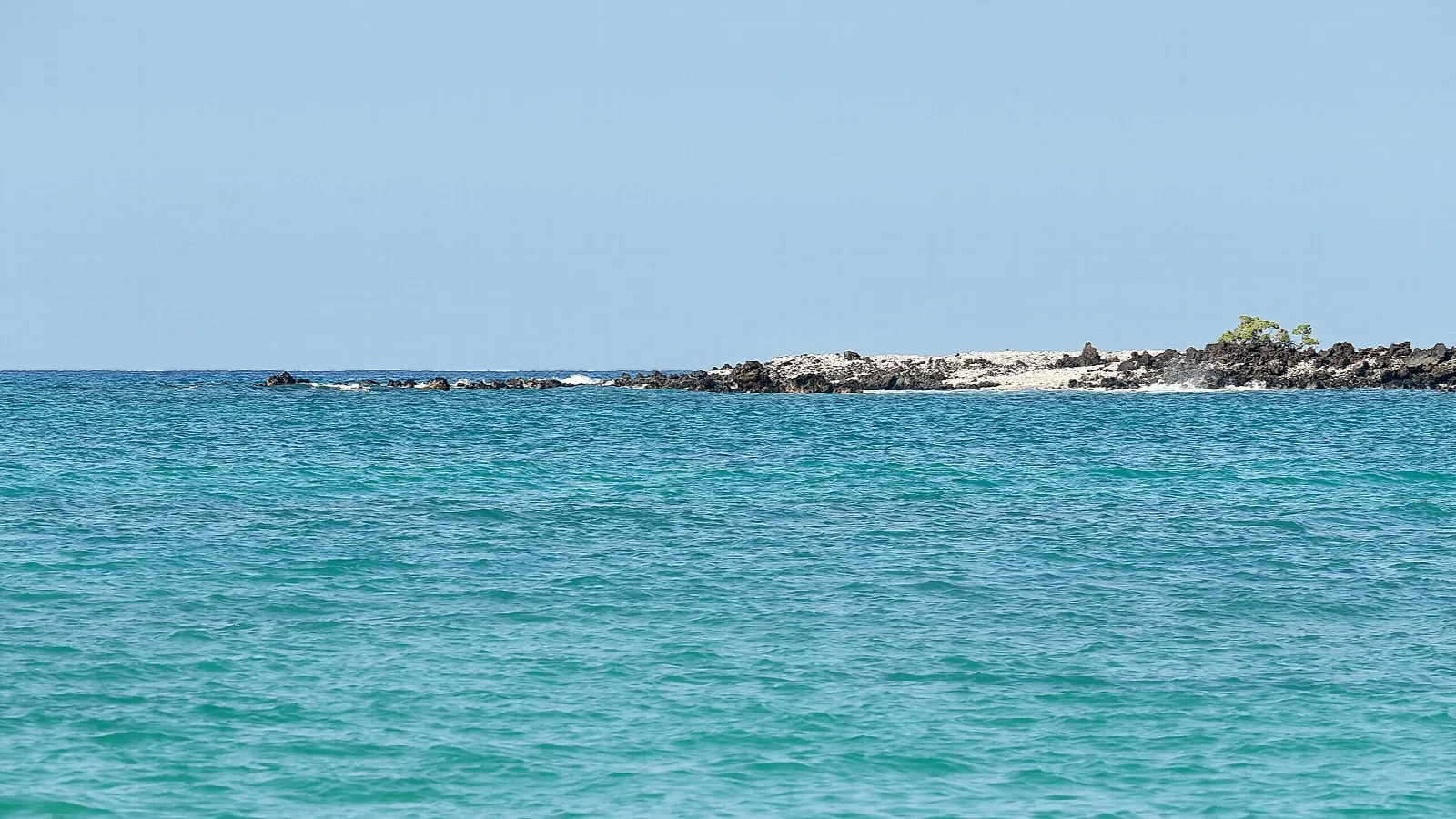 Turquoise water with a low rocky islet in the distance