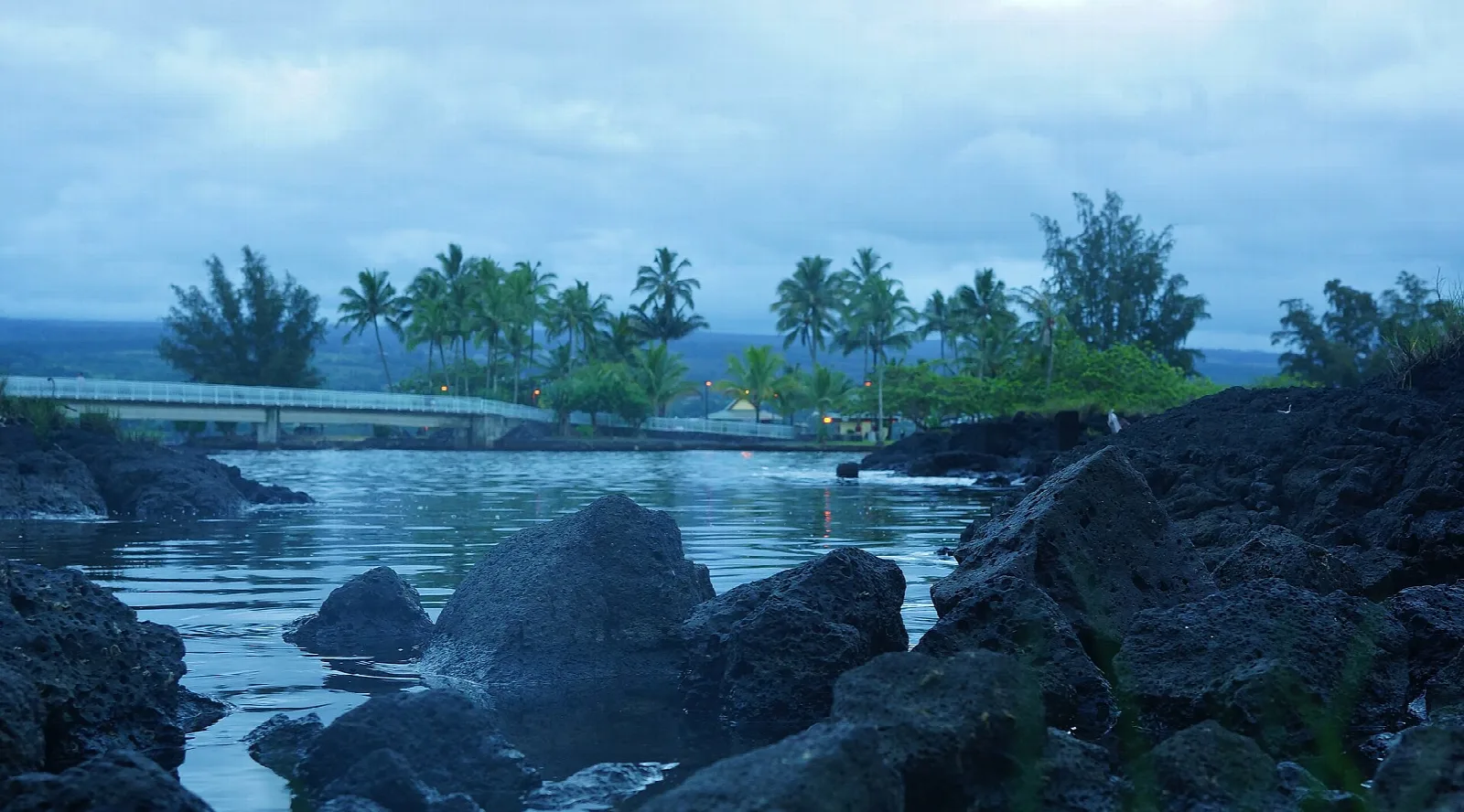 Calm pond with lava rocks in the foreground and a bridge beyond