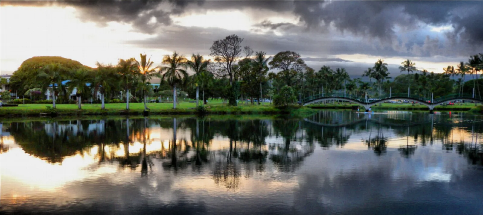 Pond at sunset with a footbridge and palms reflected in the water