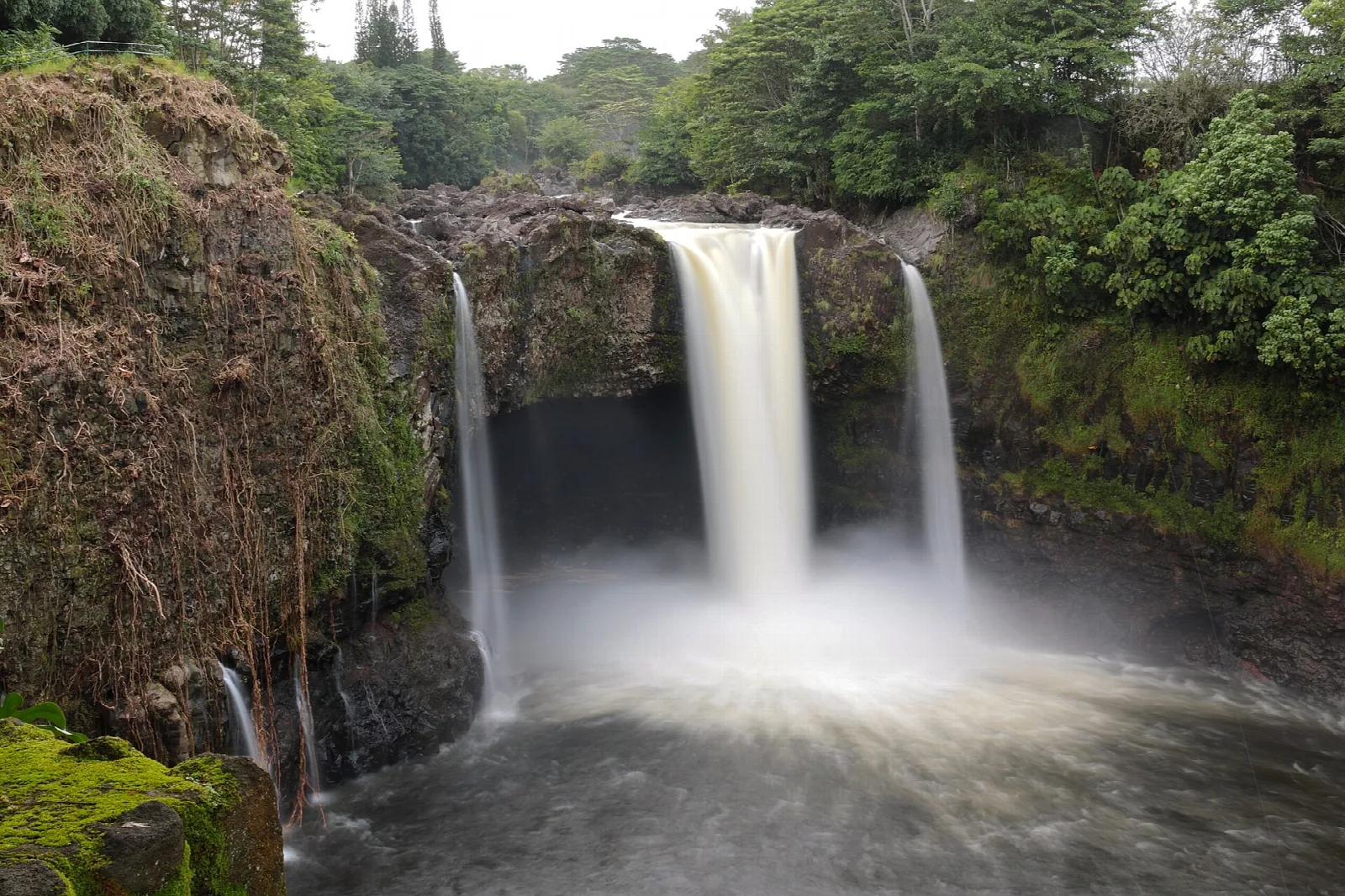 Waterfall and mist above a dark pool beside a cave