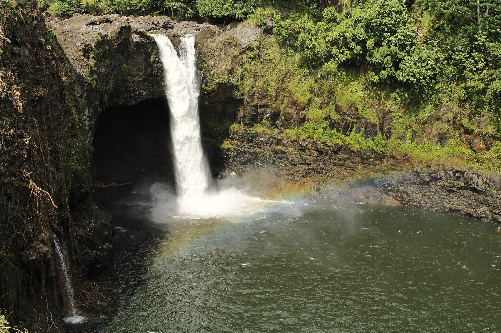 Waterfall dropping into a pool with a faint rainbow in the spray
