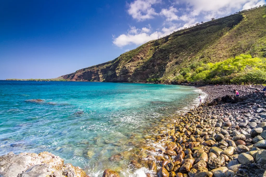 Clear turquoise bay with a steep green cliff and a rocky shoreline
