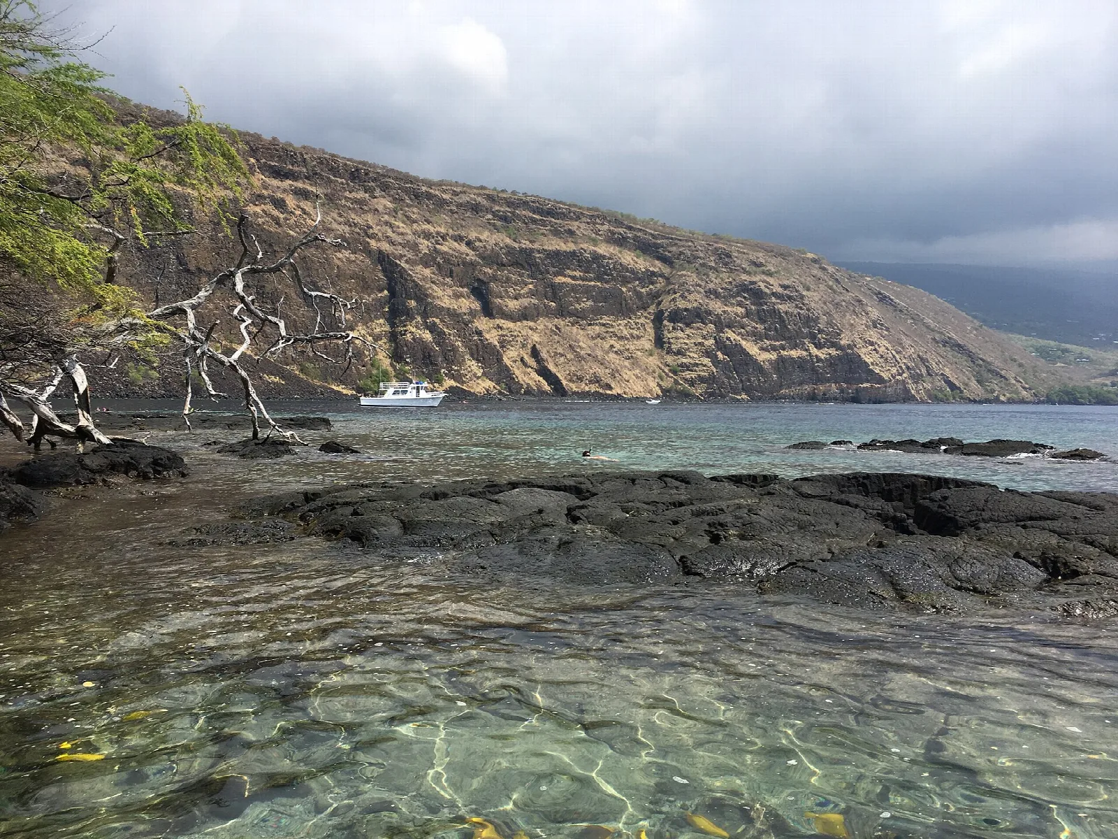 Clear shallow water over lava rock beneath a cliff