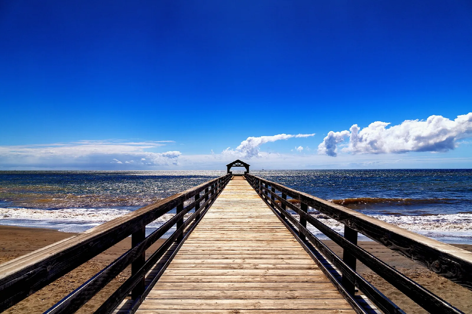A long wooden pier running out over the ocean under a blue sky