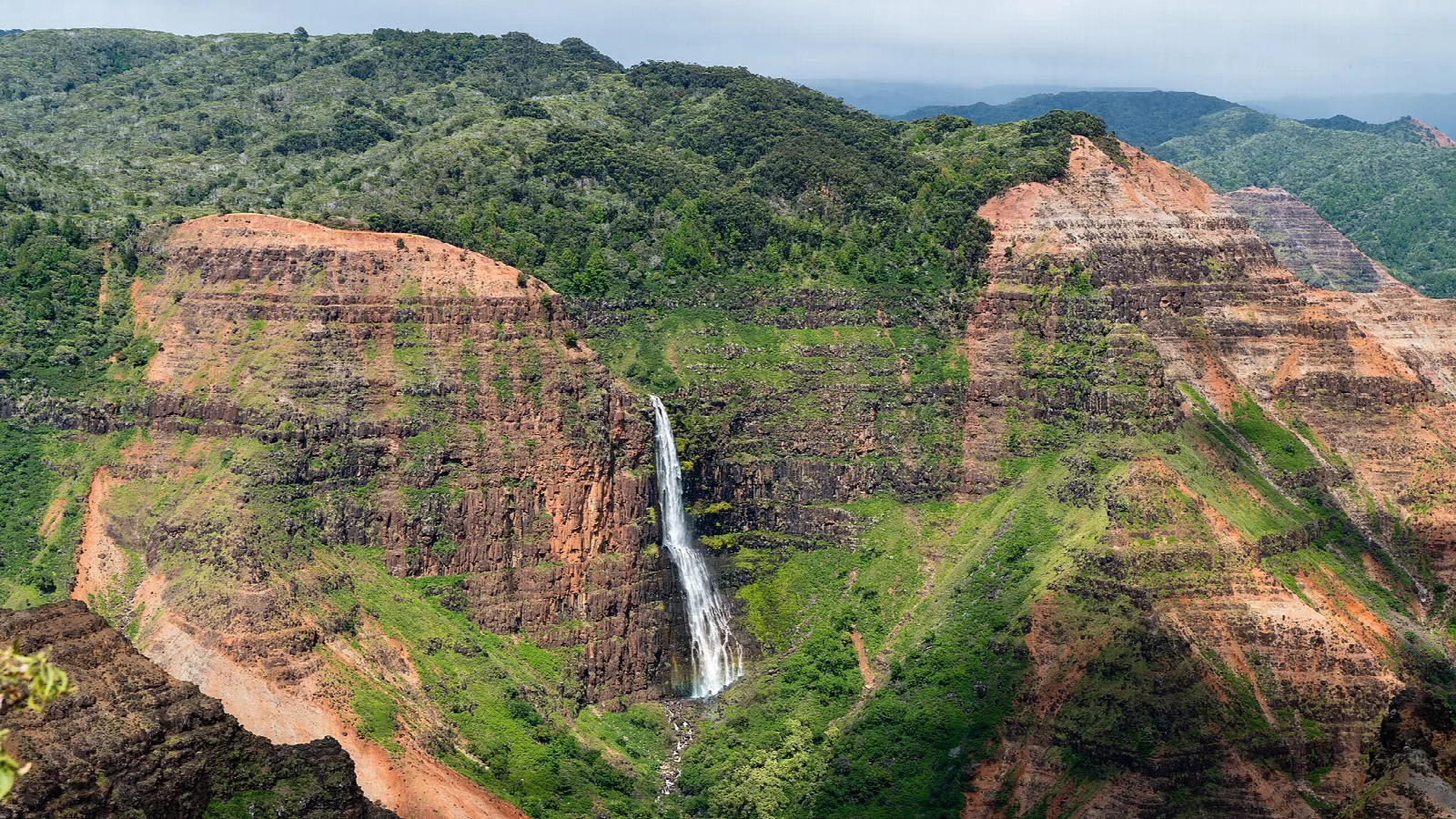 A tall waterfall dropping down a red canyon wall