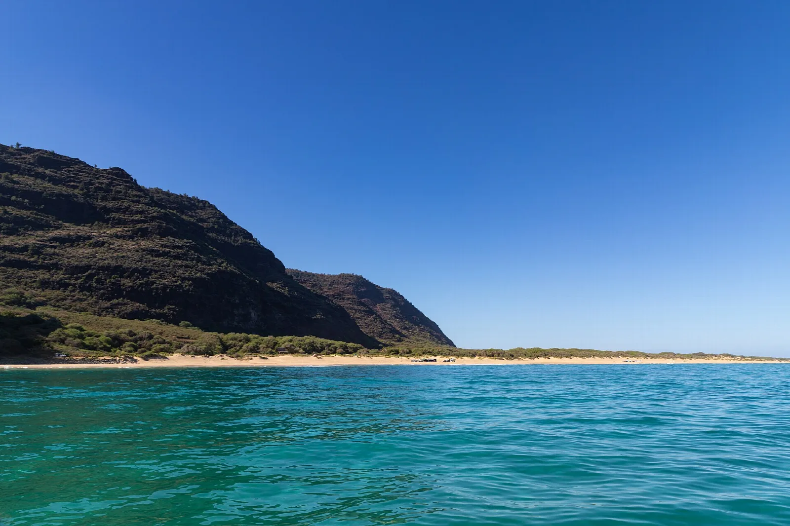 A long beach below dark cliffs beside turquoise water