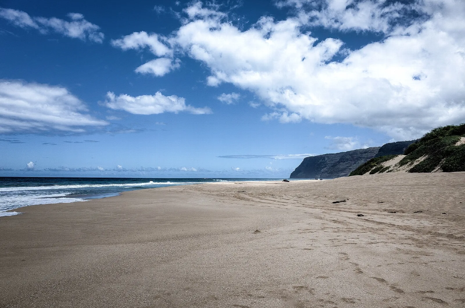 Wide sandy beach with surf on the left and a dune and cliff far down the shore