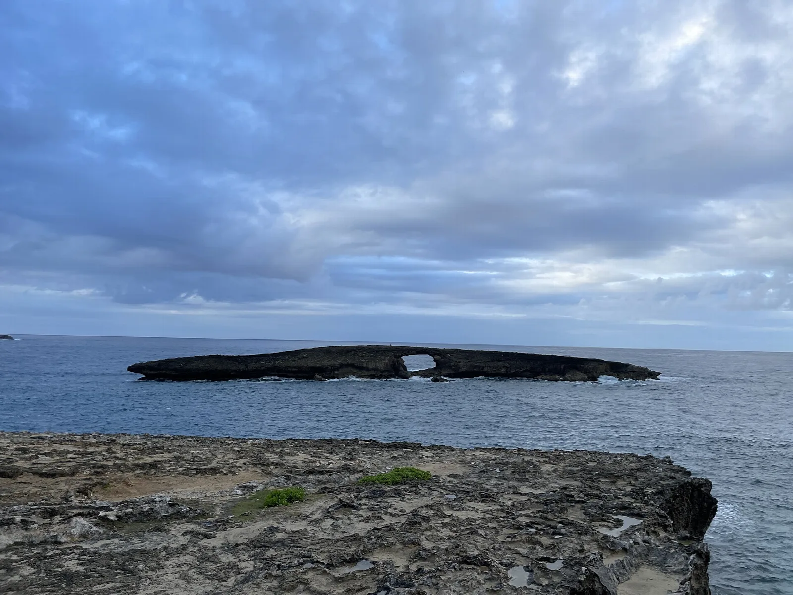 A low dark island with a sea arch across gray water