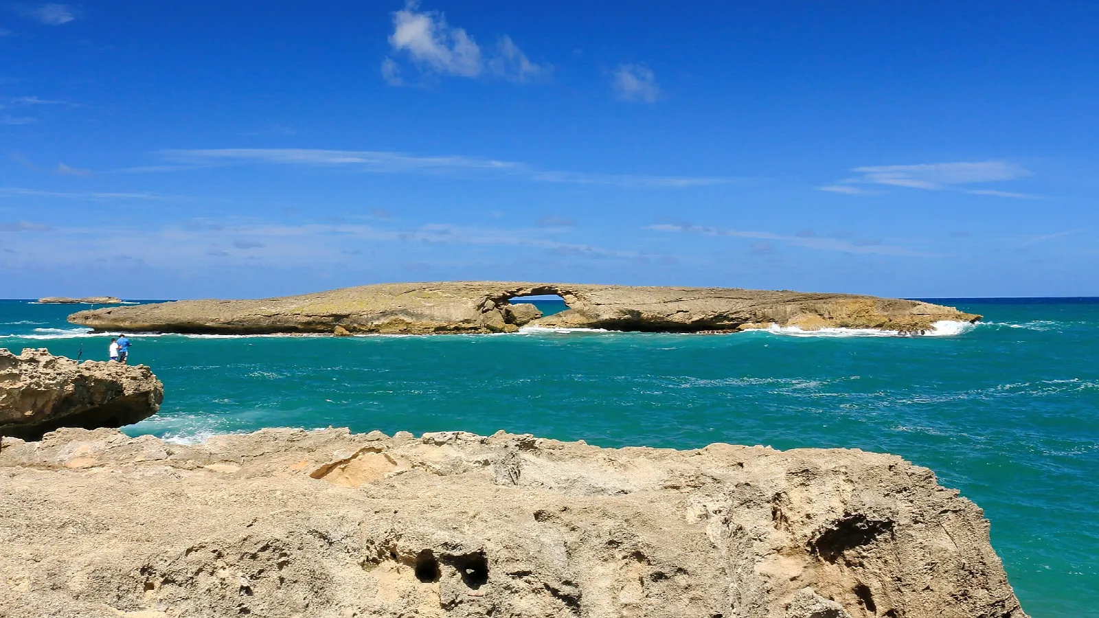 Rocky shore in the foreground and a low island with a sea arch offshore