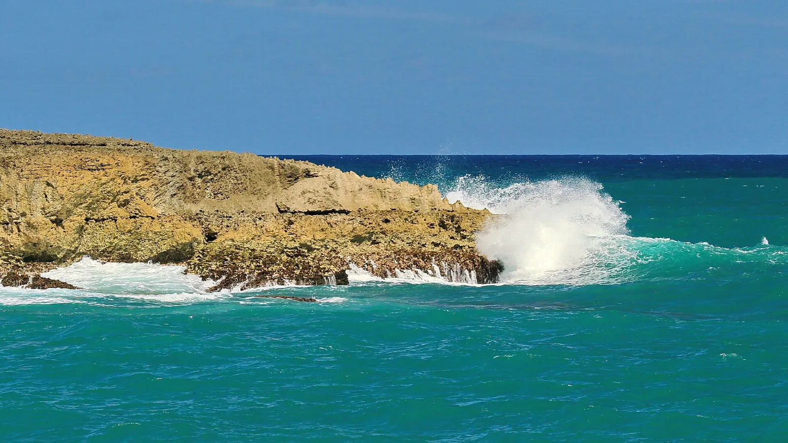 Waves crashing on a flat rock shelf over turquoise water