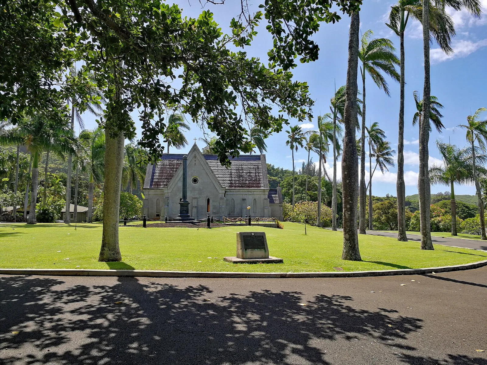 A wide lawn with tall trees and a stone chapel in the distance