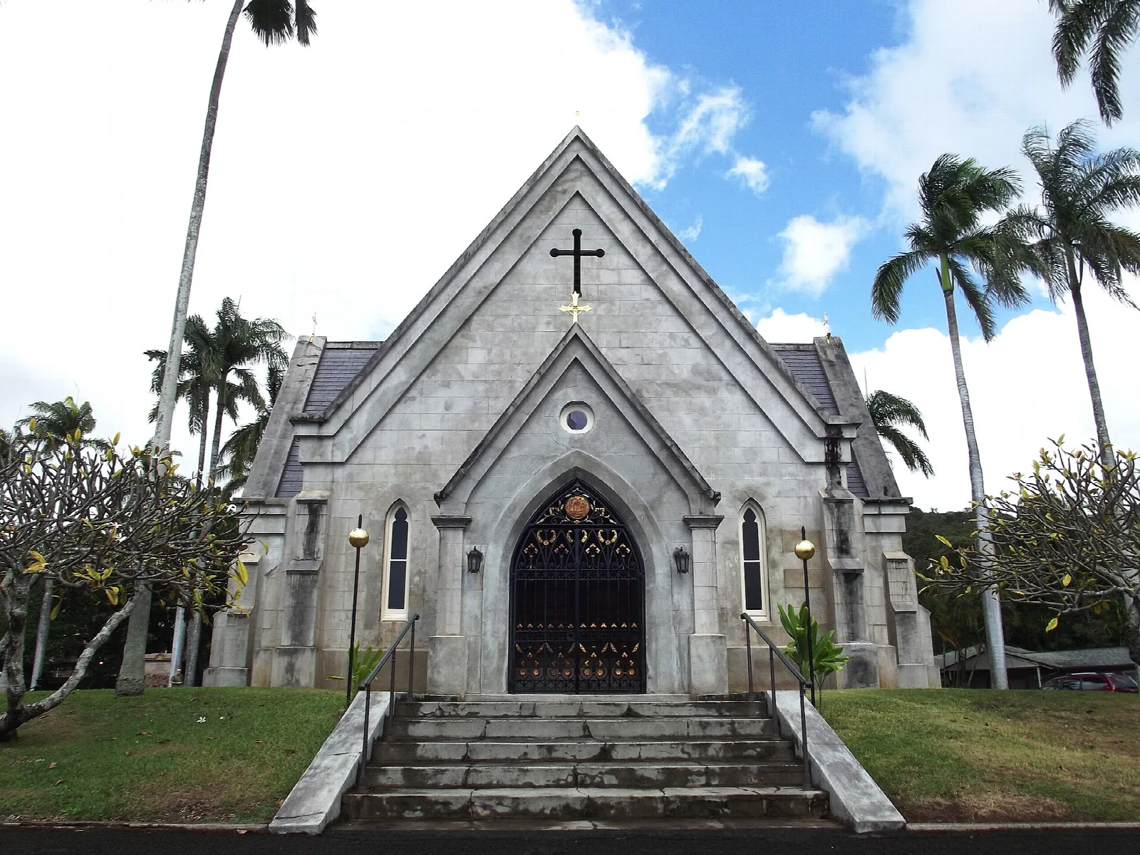 Front steps and arched door of a gray stone chapel under palms